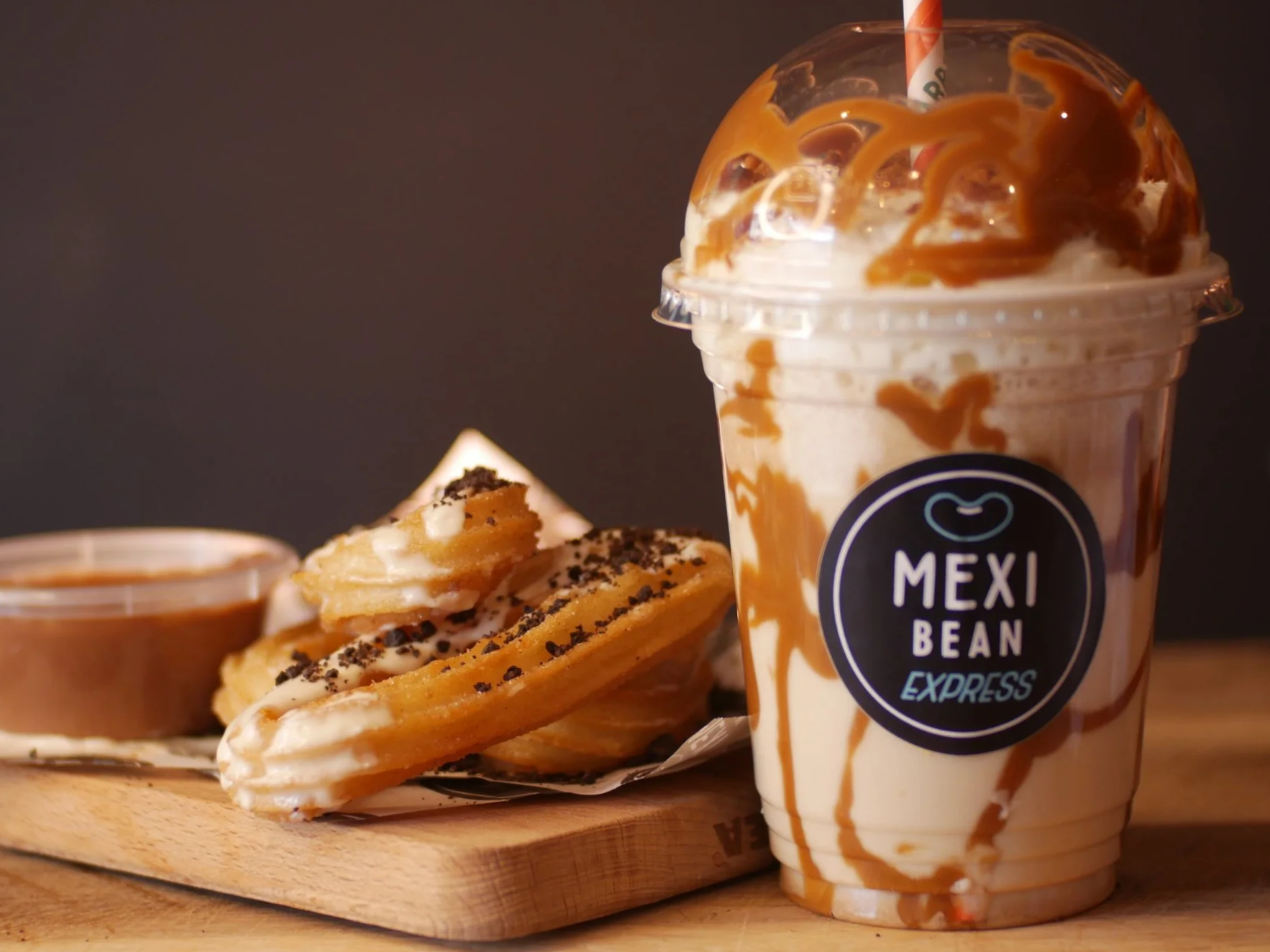 Professional food photography, taken from an online advert for a local business. Milkshake next to churros on a wooden board.