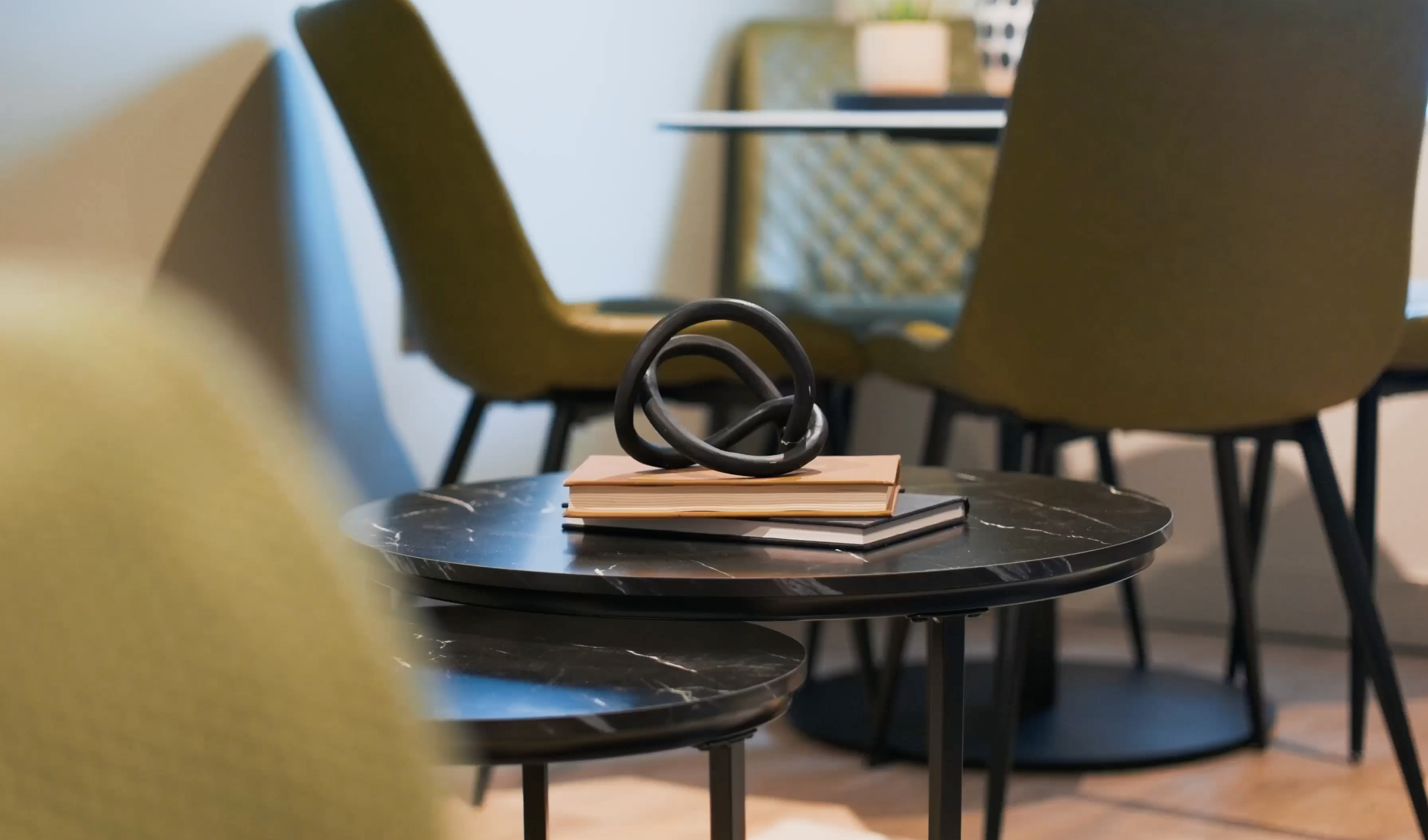 Photograph still from a property showcase video from a local Aparthotel. Modern, abstract art piece on top of a coffee table surrounded by green chairs.