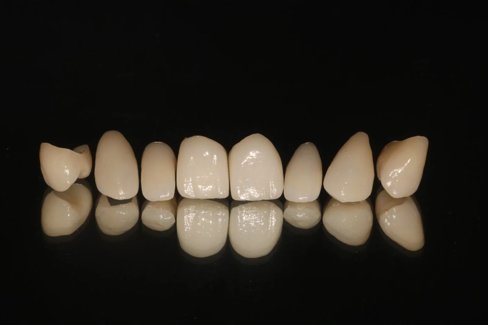 A set of artificial teeth arranged on a reflective black surface.