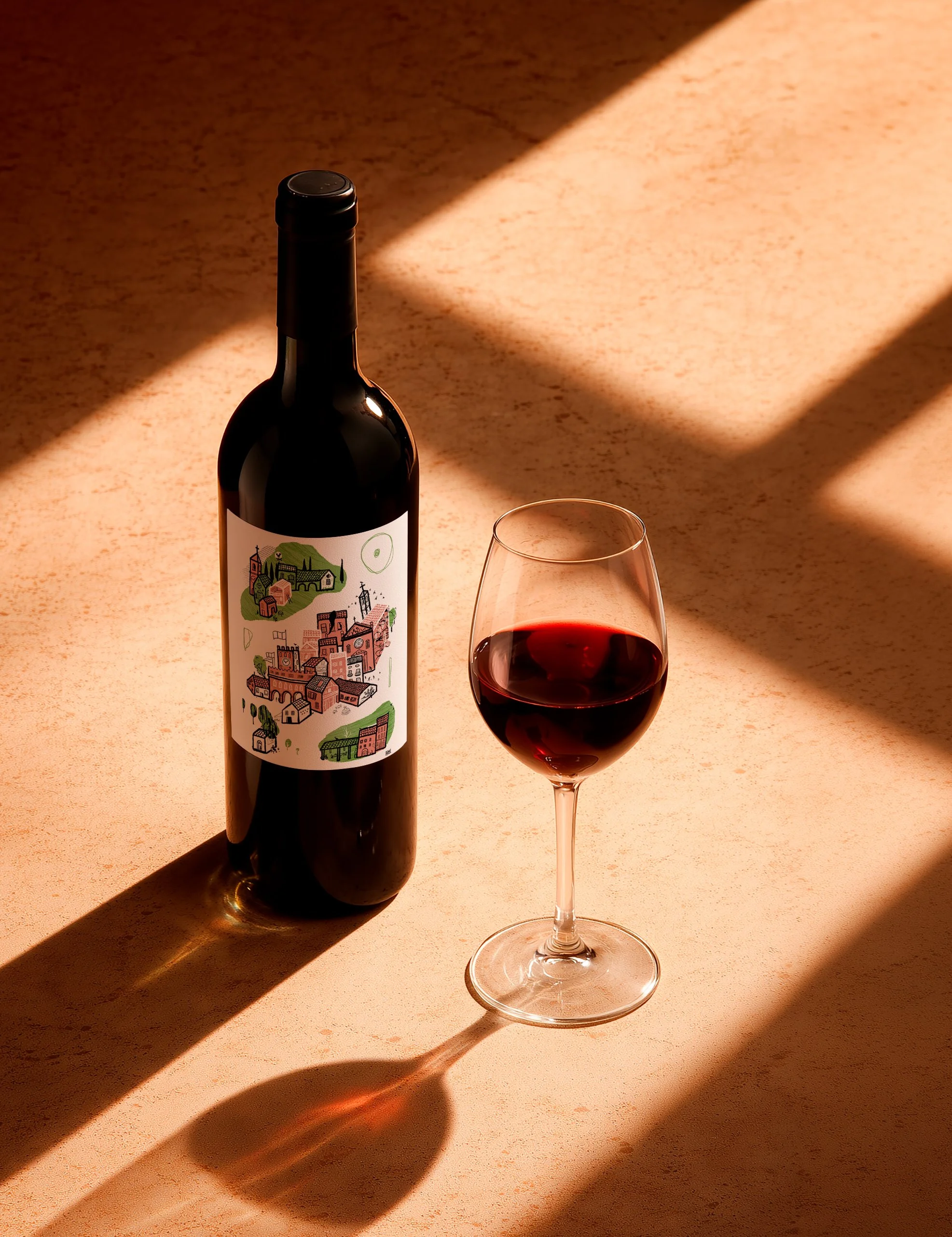 Bottiglia di vino rosso con etichetta illustrata raffigurante un borgo, fotografata accanto a un calice di vino.