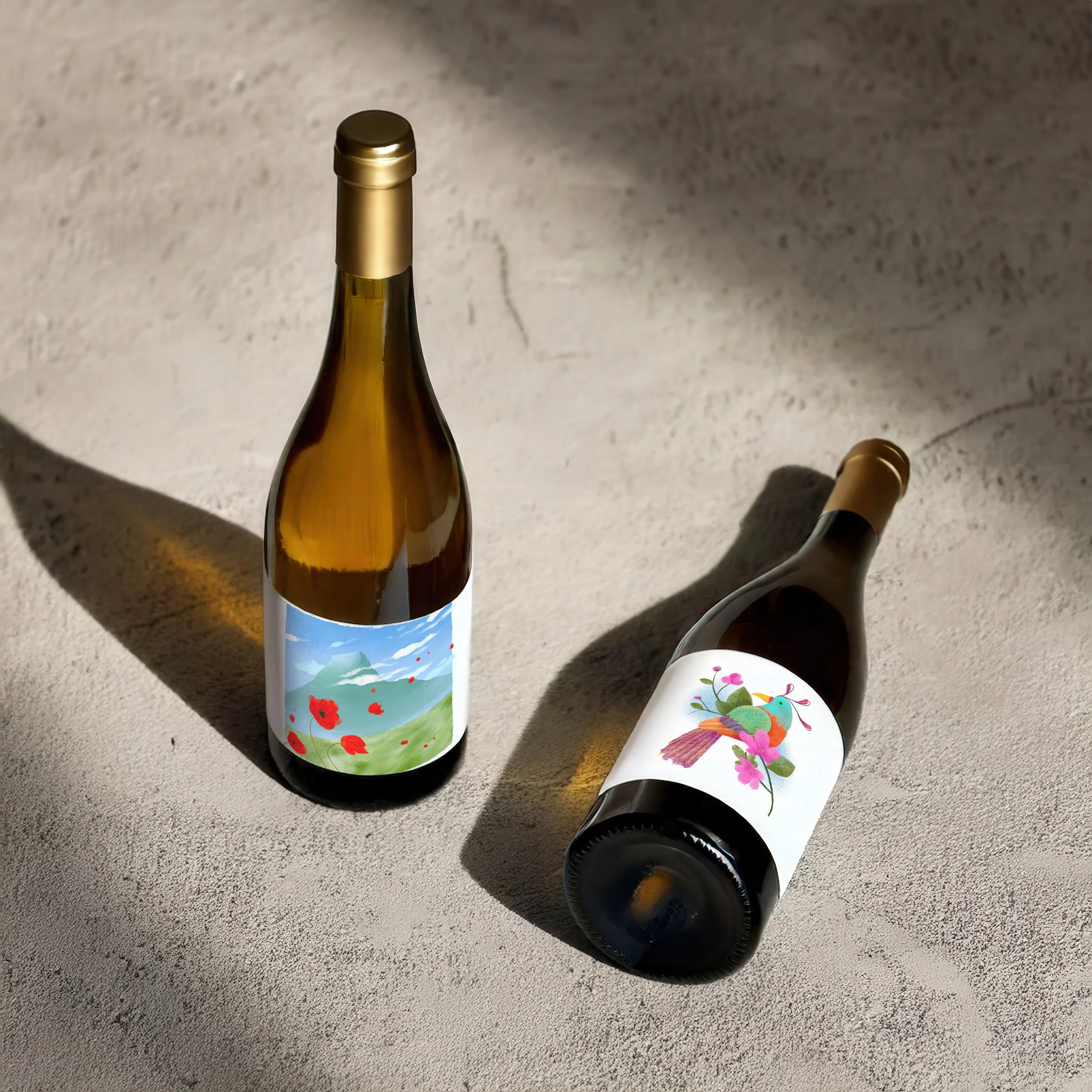 Due bottiglie di vino con etichette illustrate personalizzate, una con paesaggio e papaveri e una con illustrazione botanica e uccello.