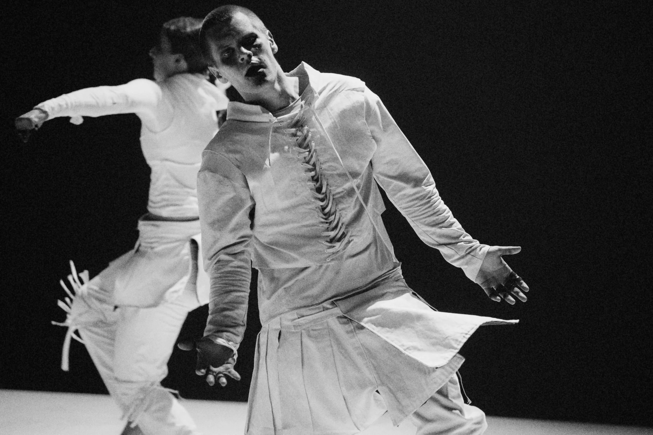 Two people practicing martial arts in a dark setting, wearing traditional white uniforms, engaging in a physical technique.