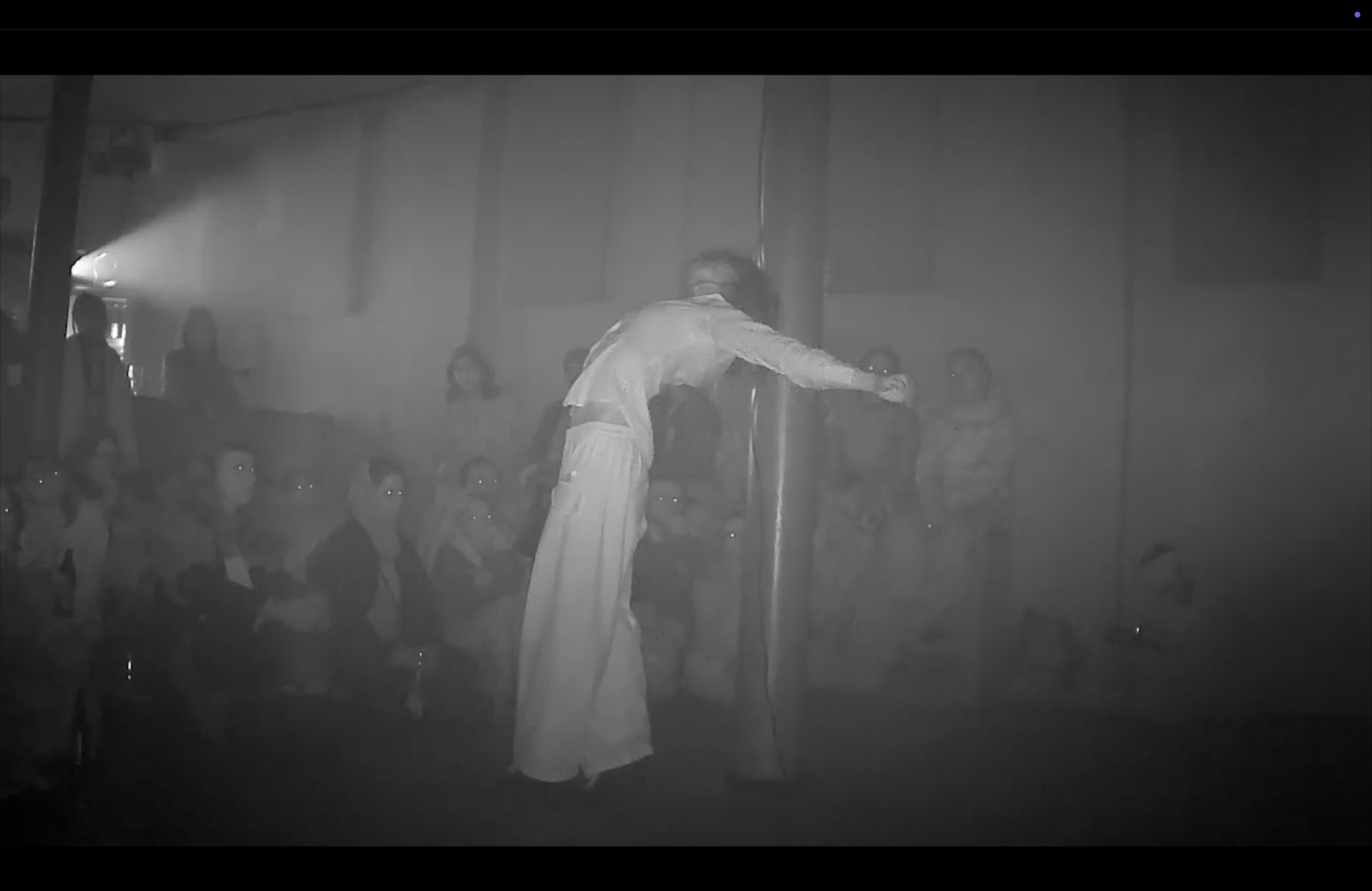 A person dressed in white performing a dance or martial arts move on a stage with an audience watching.