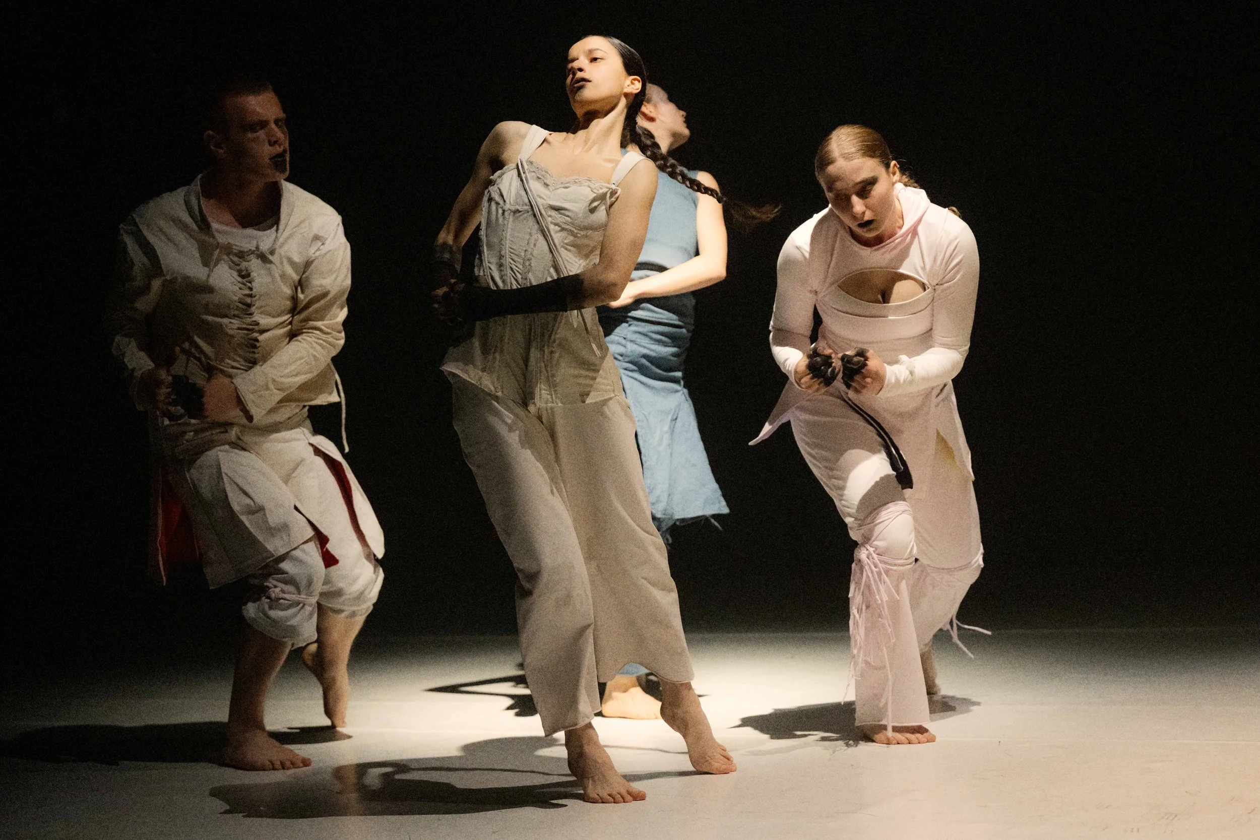Dancers performing on stage in casual clothing, barefoot, with a dark background.