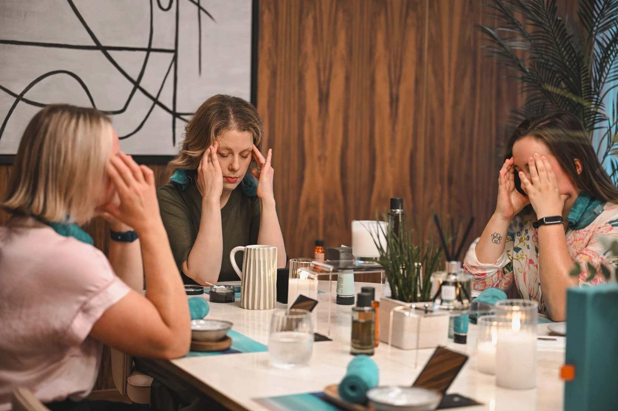 Women sitting at a table engaged in a stress-relief activity, applying face masks with various beauty products around them in a cozy, wooden-paneled room.