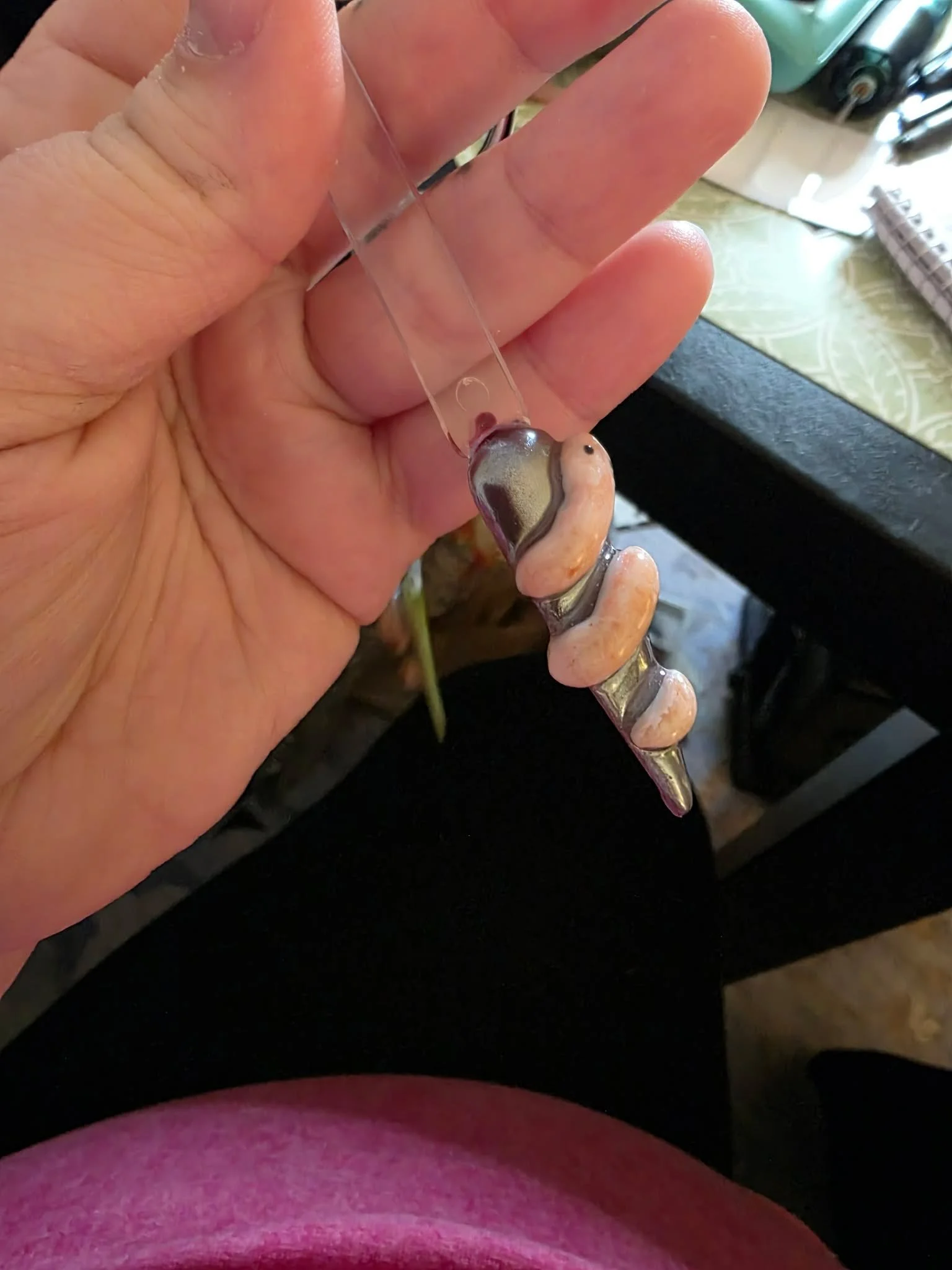 A person's hand holding a small fish with a hook in its mouth, near a green plant and a pink garment.