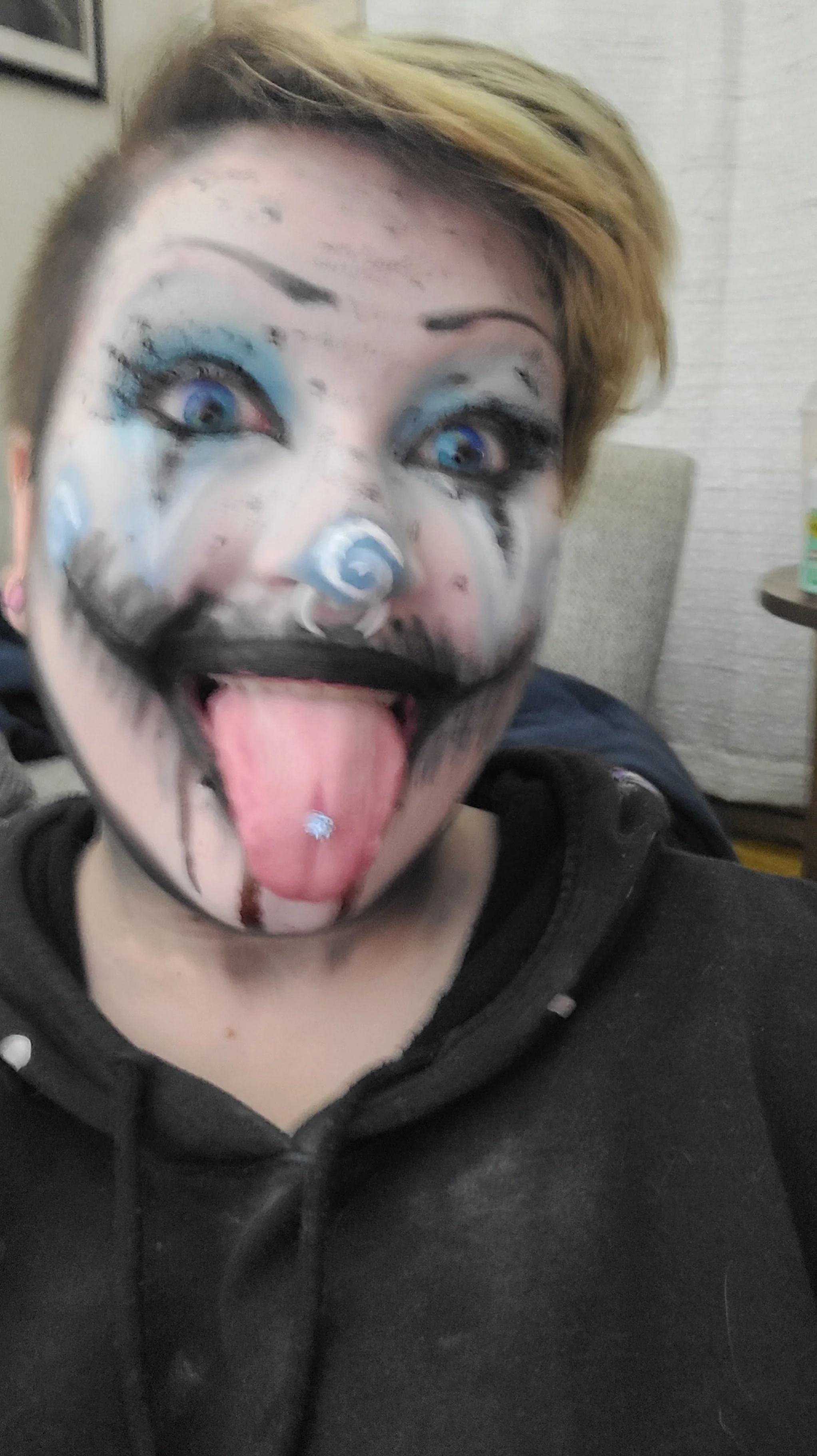 Person with clown makeup taking a selfie, sticking out their tongue, and wearing a black hoodie.
