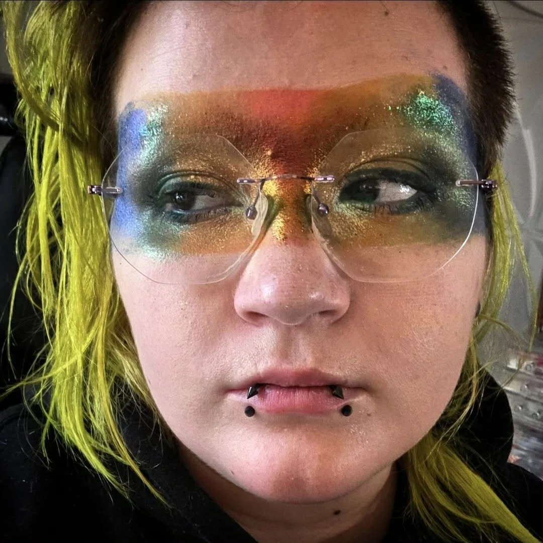 A person with yellow-green dyed hair wearing rainbow pride makeup