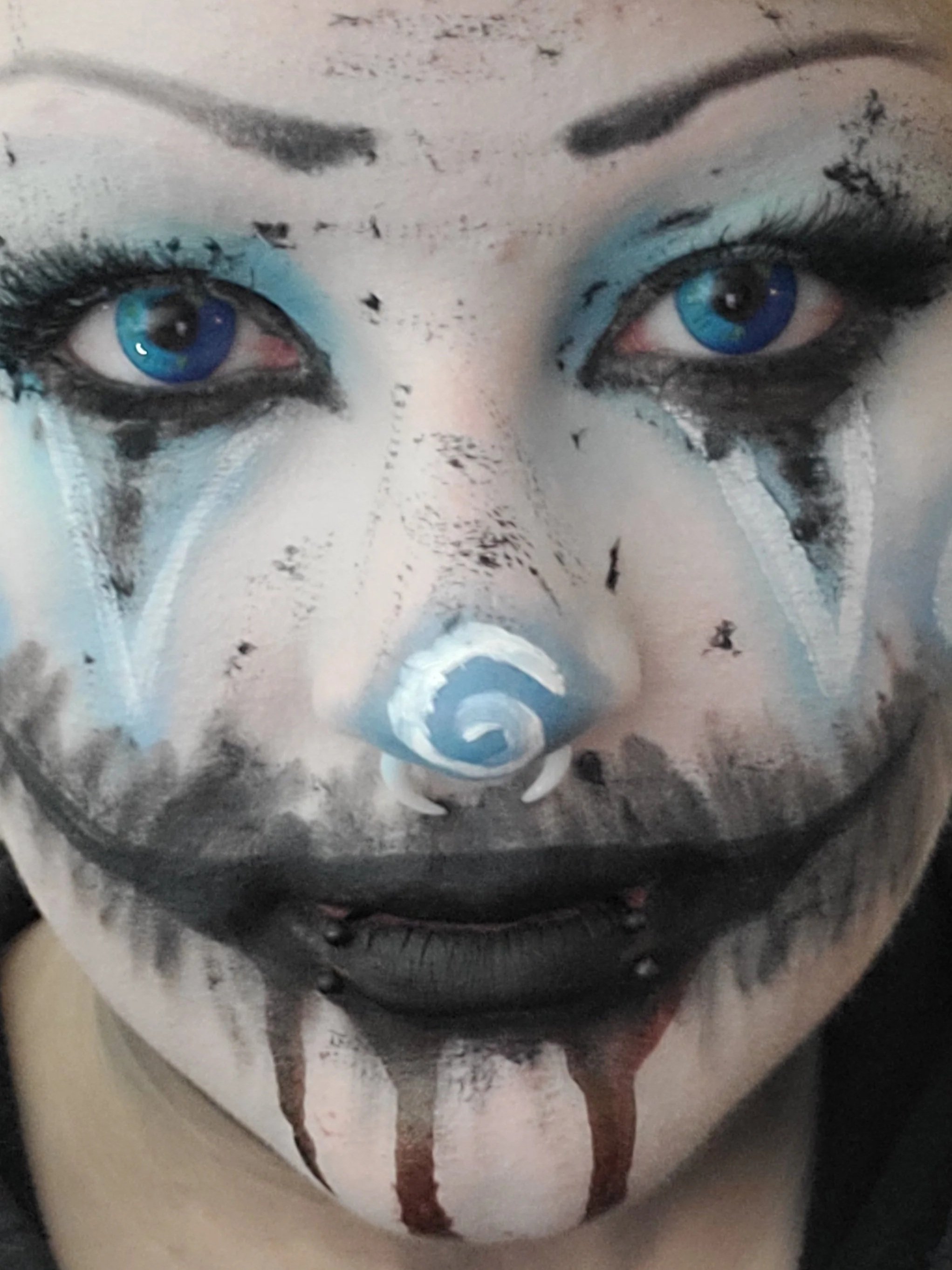 Close-up of a person's eyes and nose painted to resemble a clown, with blue eye makeup and black details, and streaks running down the face.