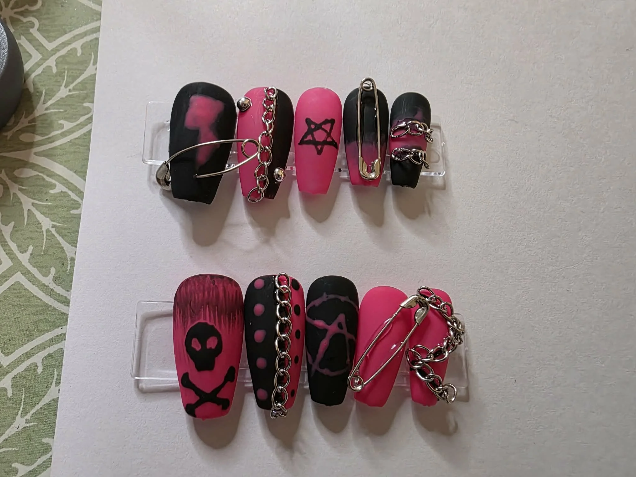 A collection of hair clips on a white display stand, featuring black and pink colors with skull and star designs, some embellished with chains or metal accents.