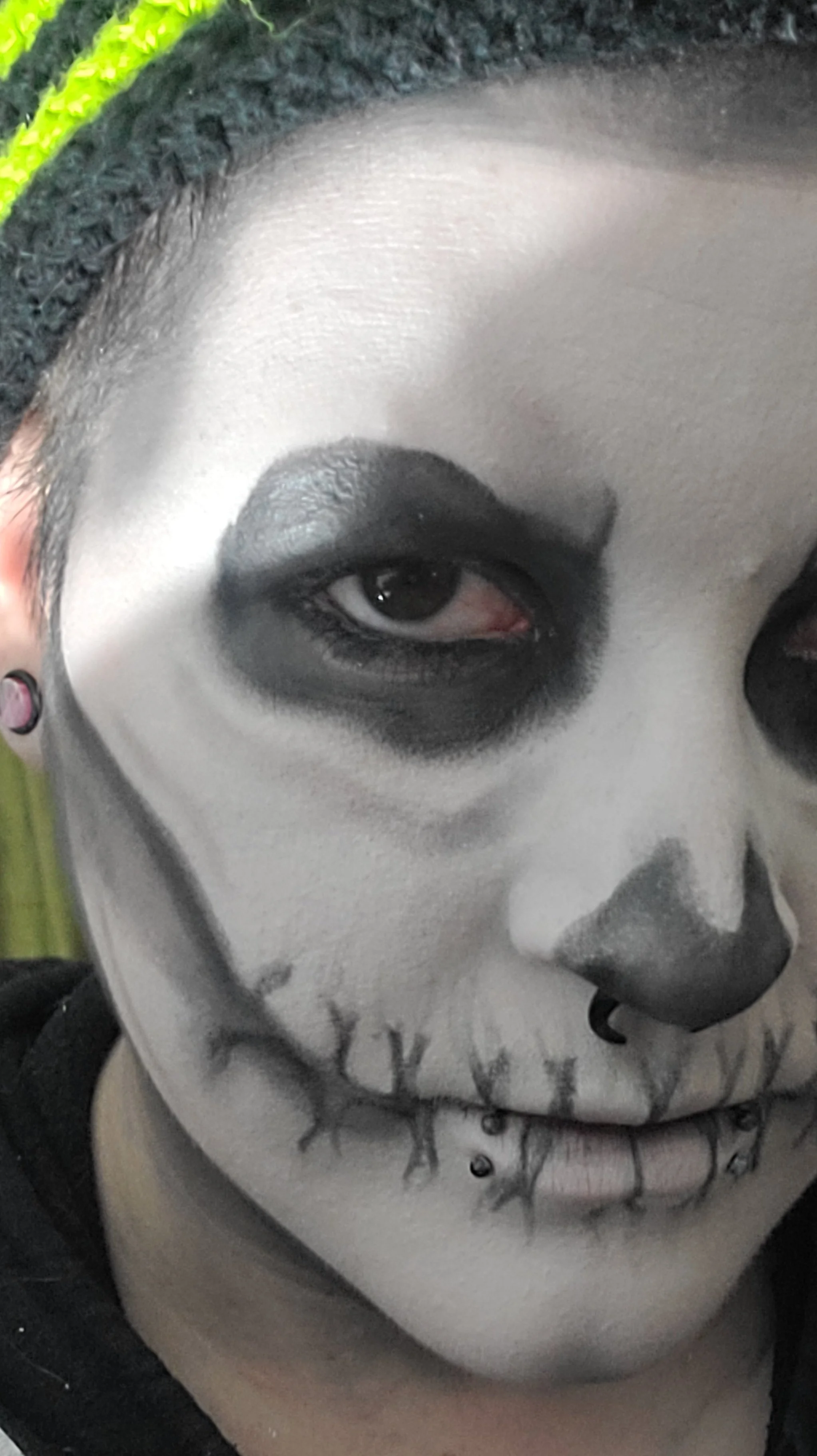 Close-up of a person with white skull makeup, black eye makeup, and a black nose painted on their face.