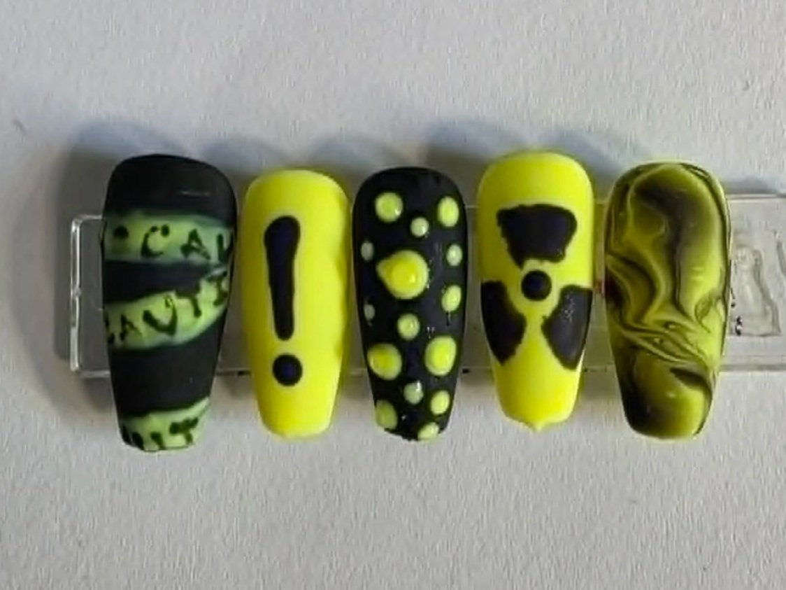 Five artificial nails painted in yellow and black with various patterns and designs.