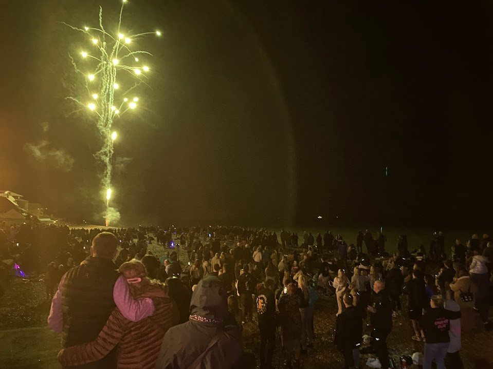 Crowd of people on a beach watching fireworks at night.