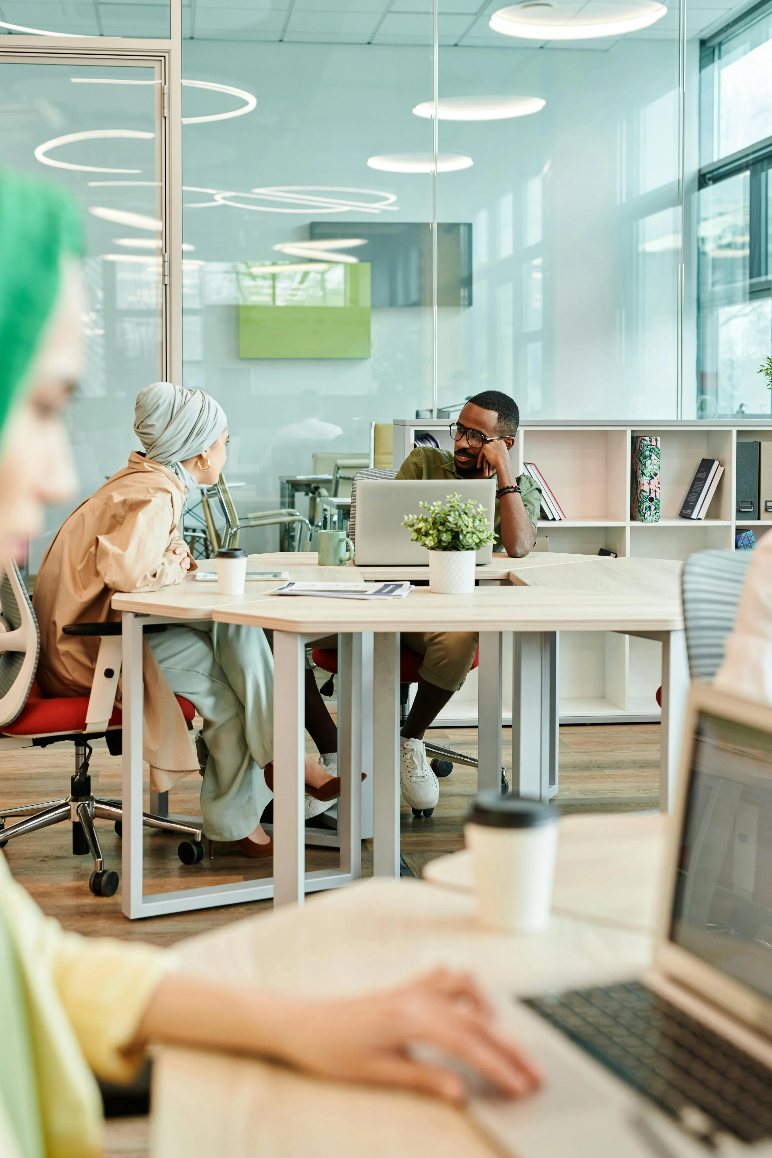 People having a discussion in a modern office conference room with glass walls, bookshelves, and contemporary lighting.