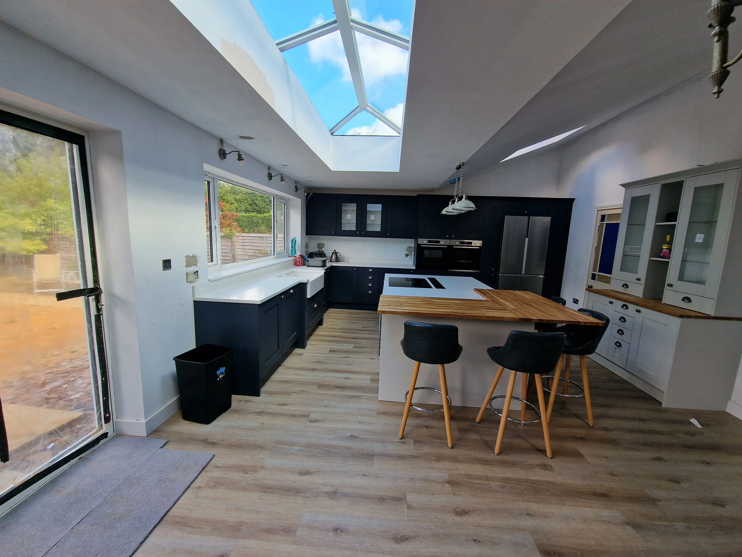 Kitchen with blue cabinets, white countertops, a butcher block island, and a skylight ceiling showing part of a blue sky with clouds.