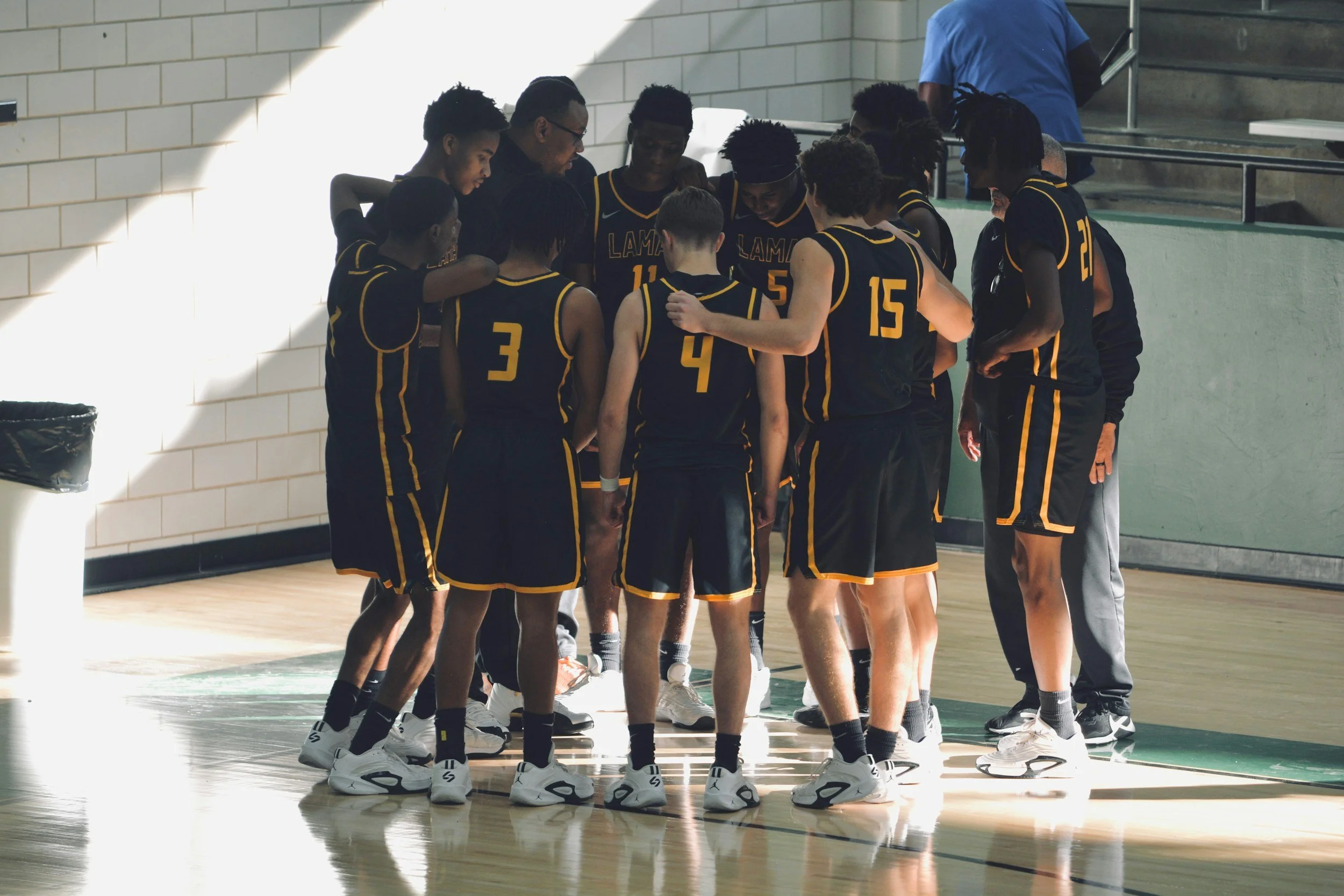 A basketball team huddles together on the court during a timeout in a game.
