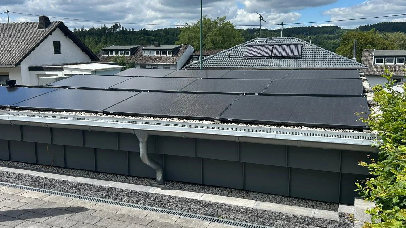 Dach mit Solarzellen und Dachrinne, umgeben von anderen Häusern und Bäumen in einer ländlichen Gegend