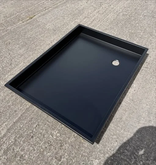 Black metal shower tray with a round drain hole, placed on concrete ground.