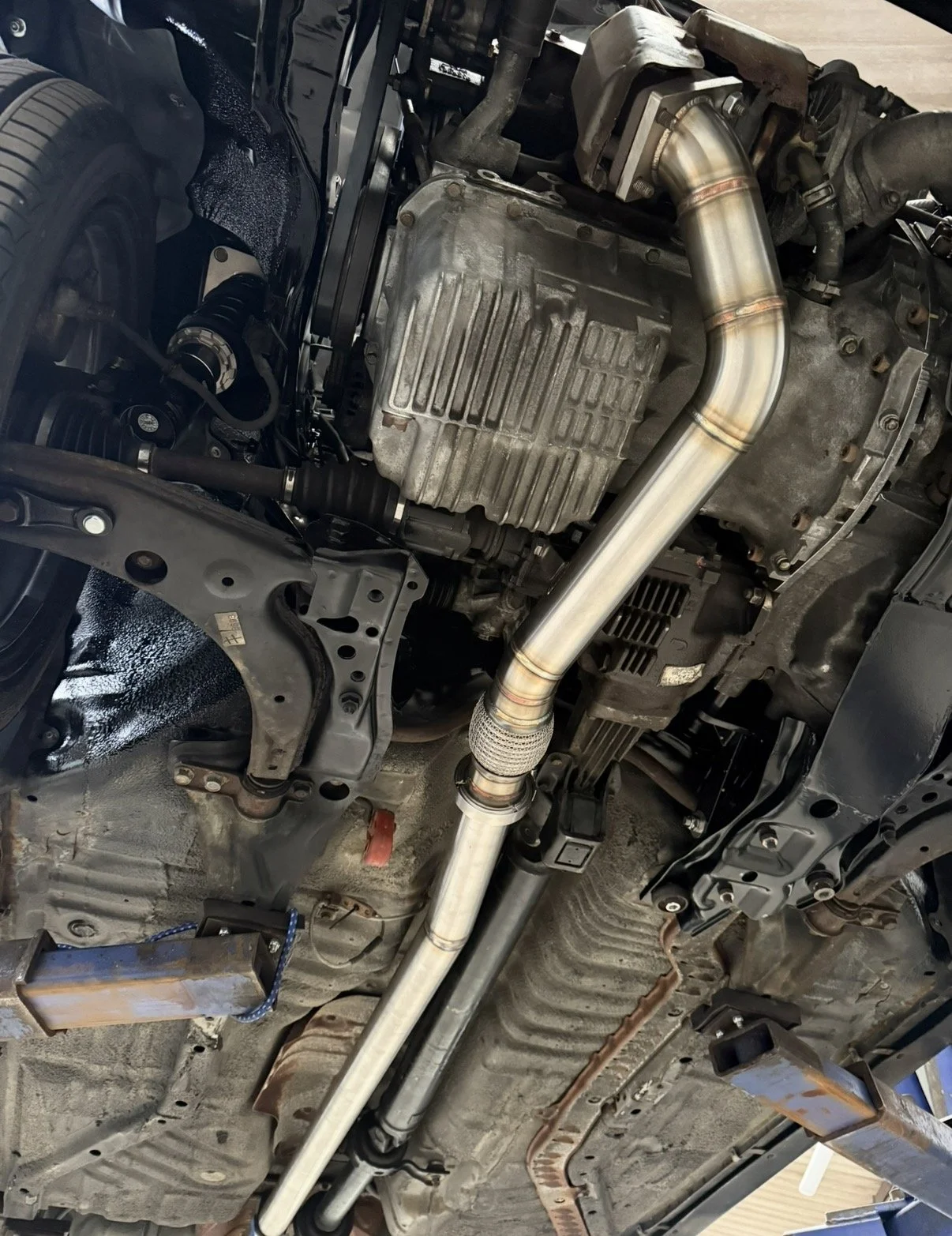 Underneath view of a car's engine and exhaust system, including the oil pan, pipes, and various mechanical parts.