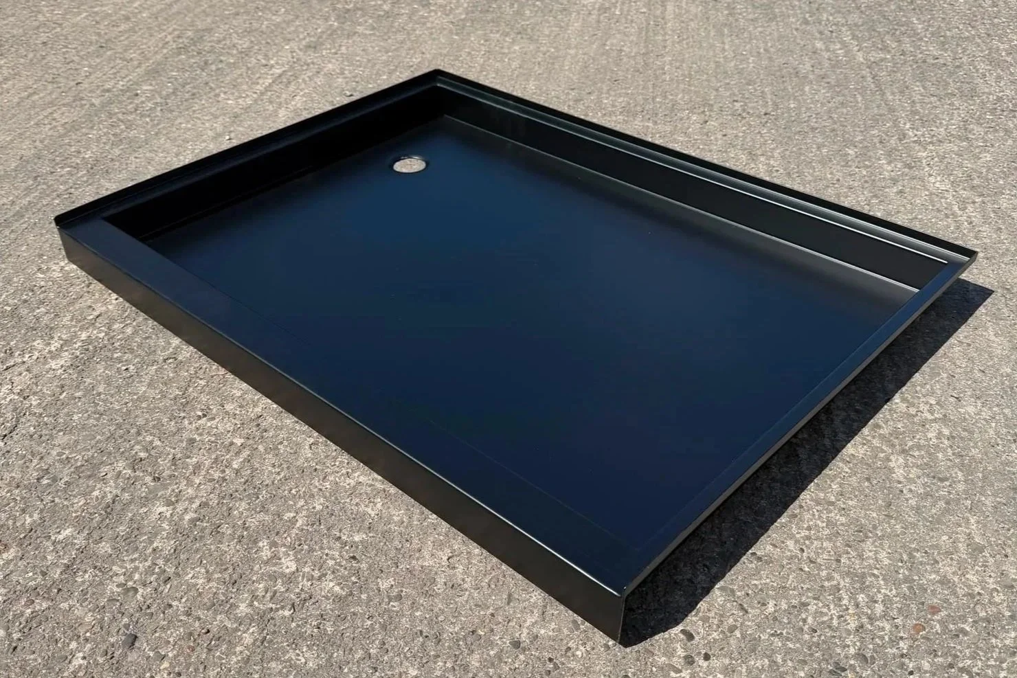 Black metal tray with a small circular hole in one corner, placed on a gray concrete surface.