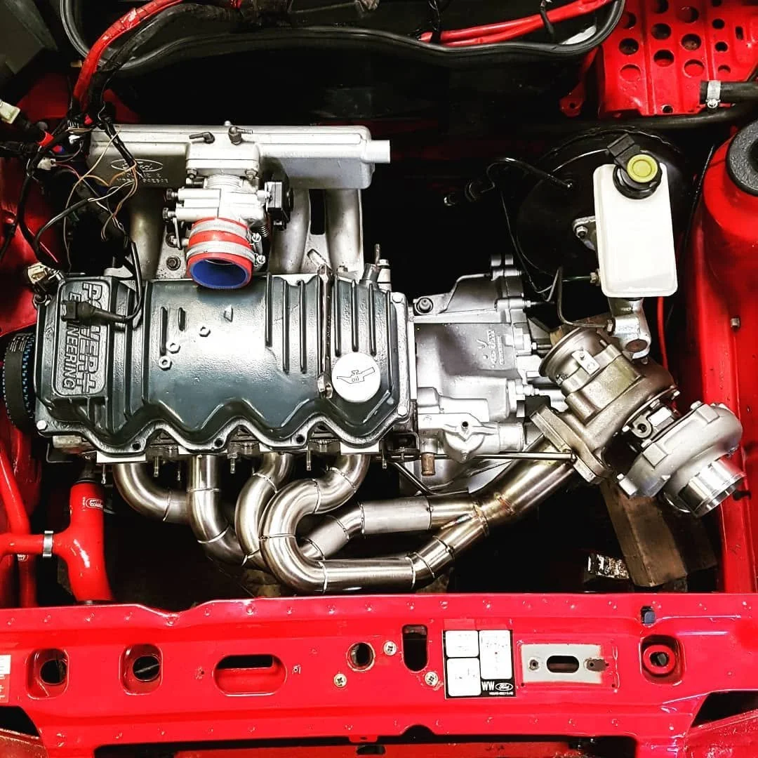 A close-up view of a car engine with various metallic parts, hoses, and wires, installed in a red engine bay.