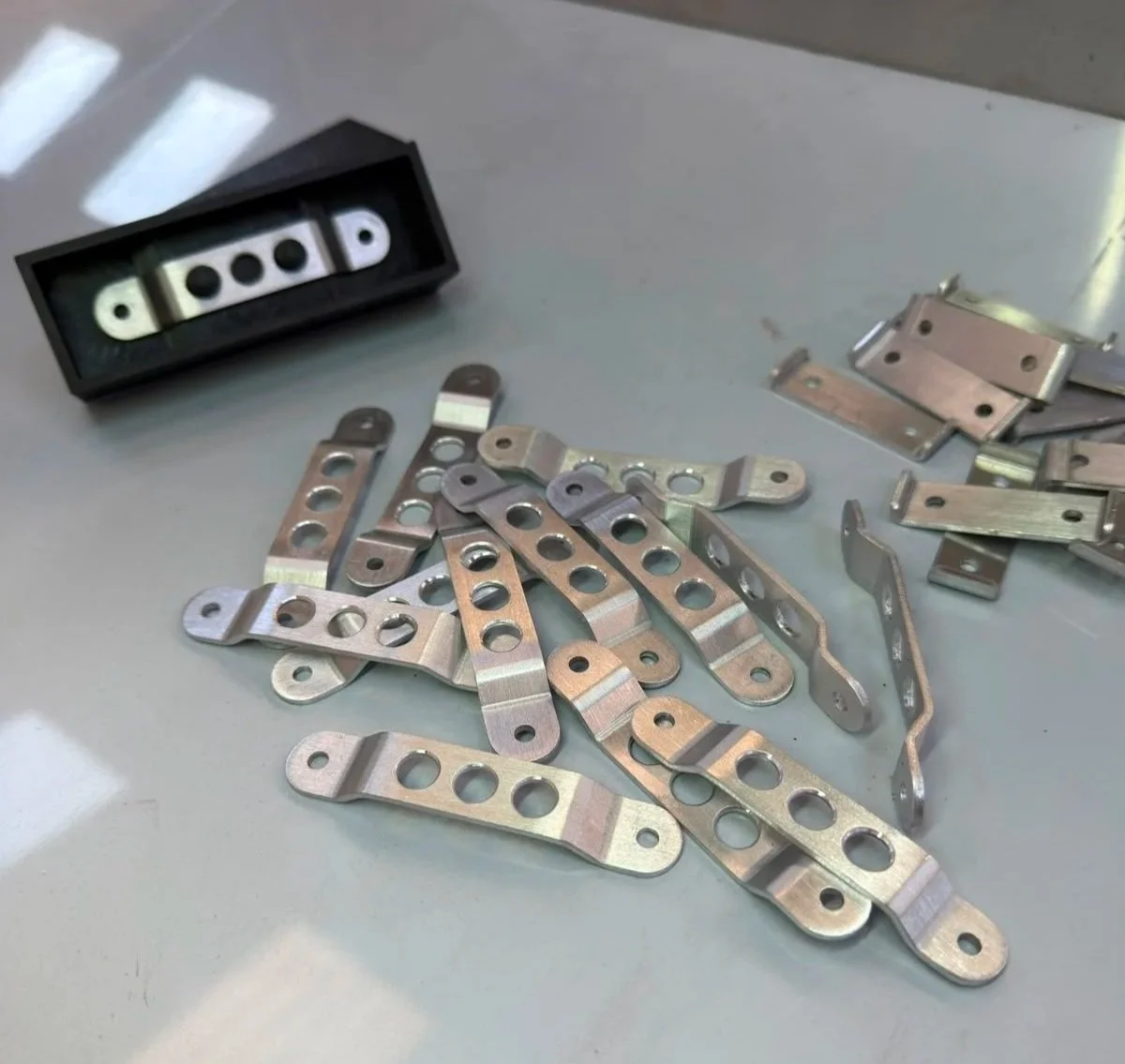 Various metal hinges and a small black box with white parts and black holes, placed on a light-colored surface.