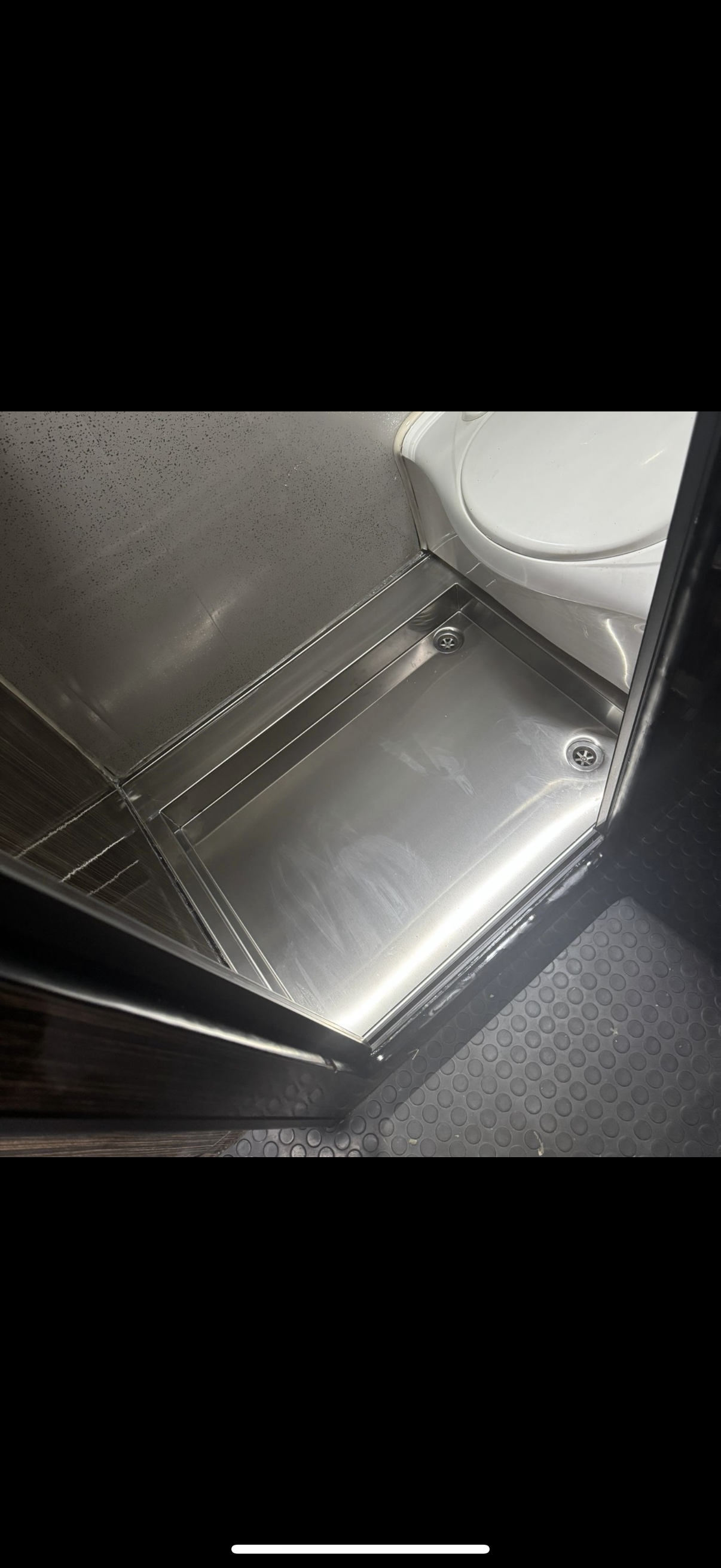 Empty stainless steel shower stall with a white toilet in the corner.