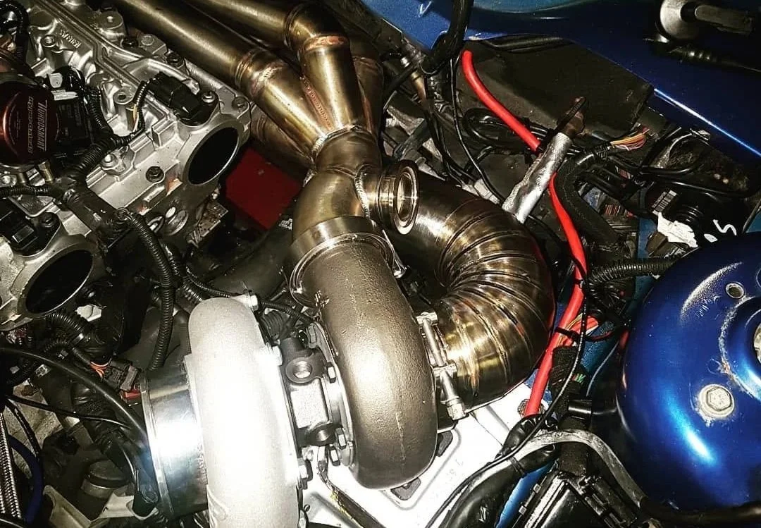 Close-up of a turbocharger installed in a car engine with visible exhaust piping and wiring.