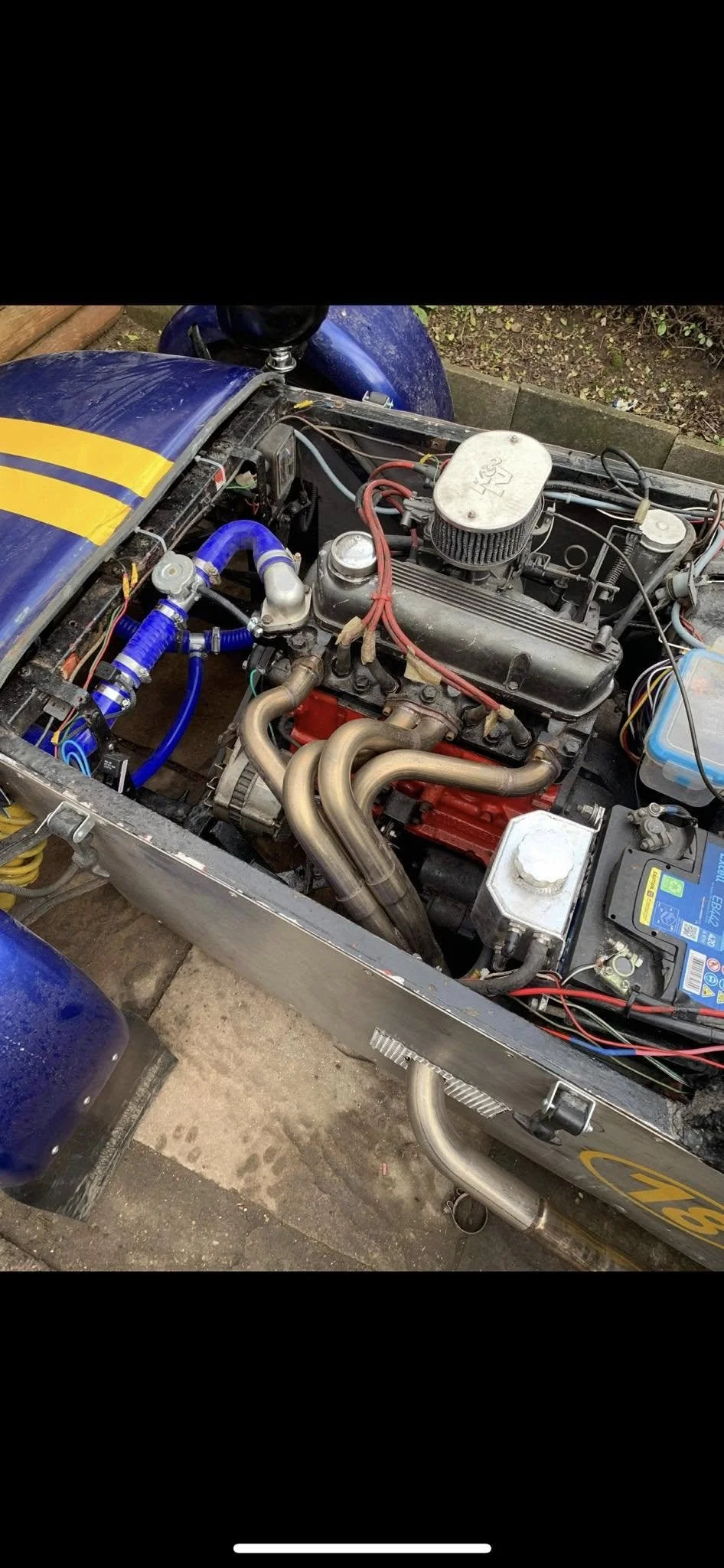 Close-up of a car engine inside a race car with blue and yellow exterior, showing the engine, exhaust pipes, and wiring.