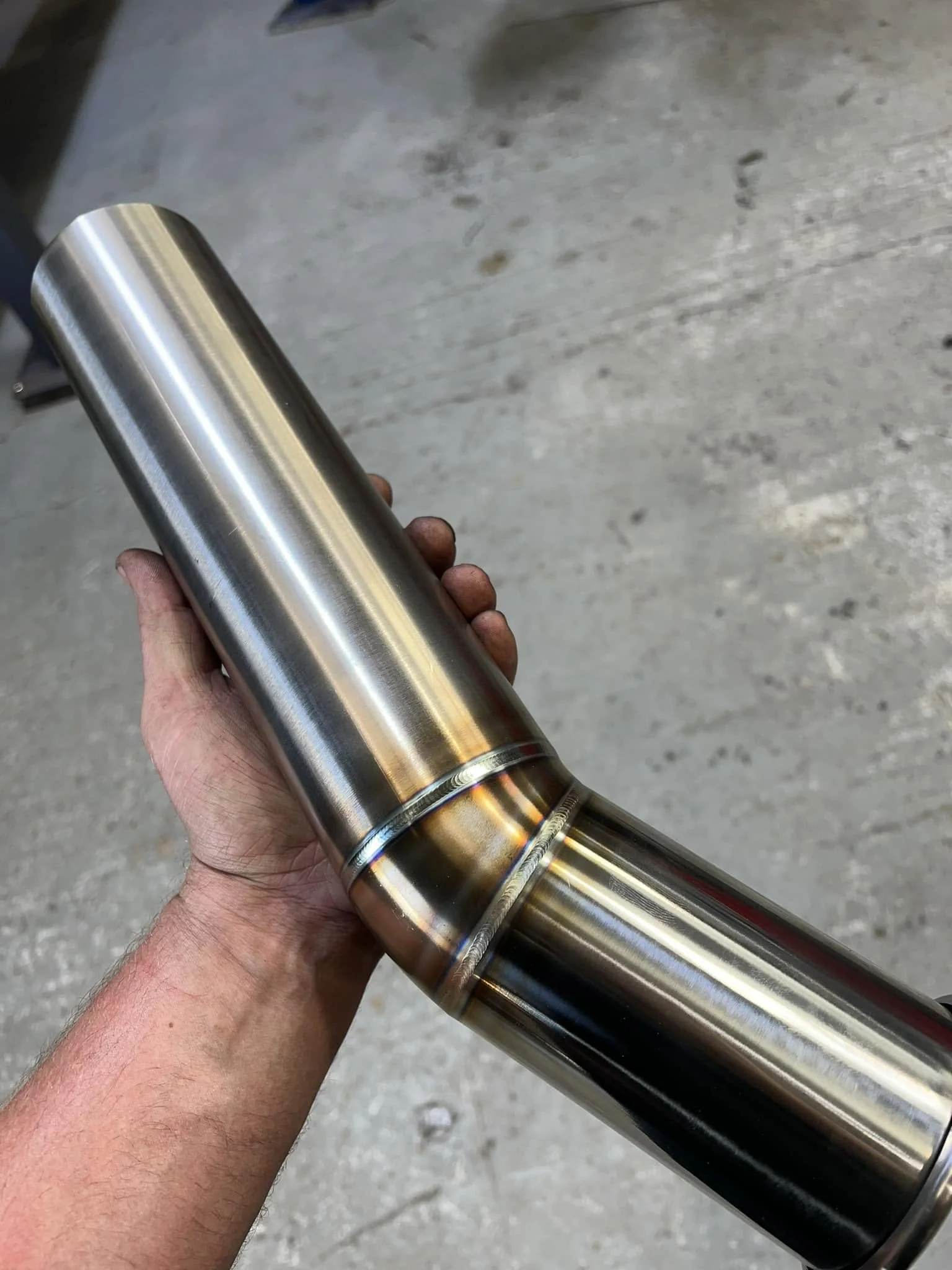 Hand holding a metallic, polished exhaust pipe.