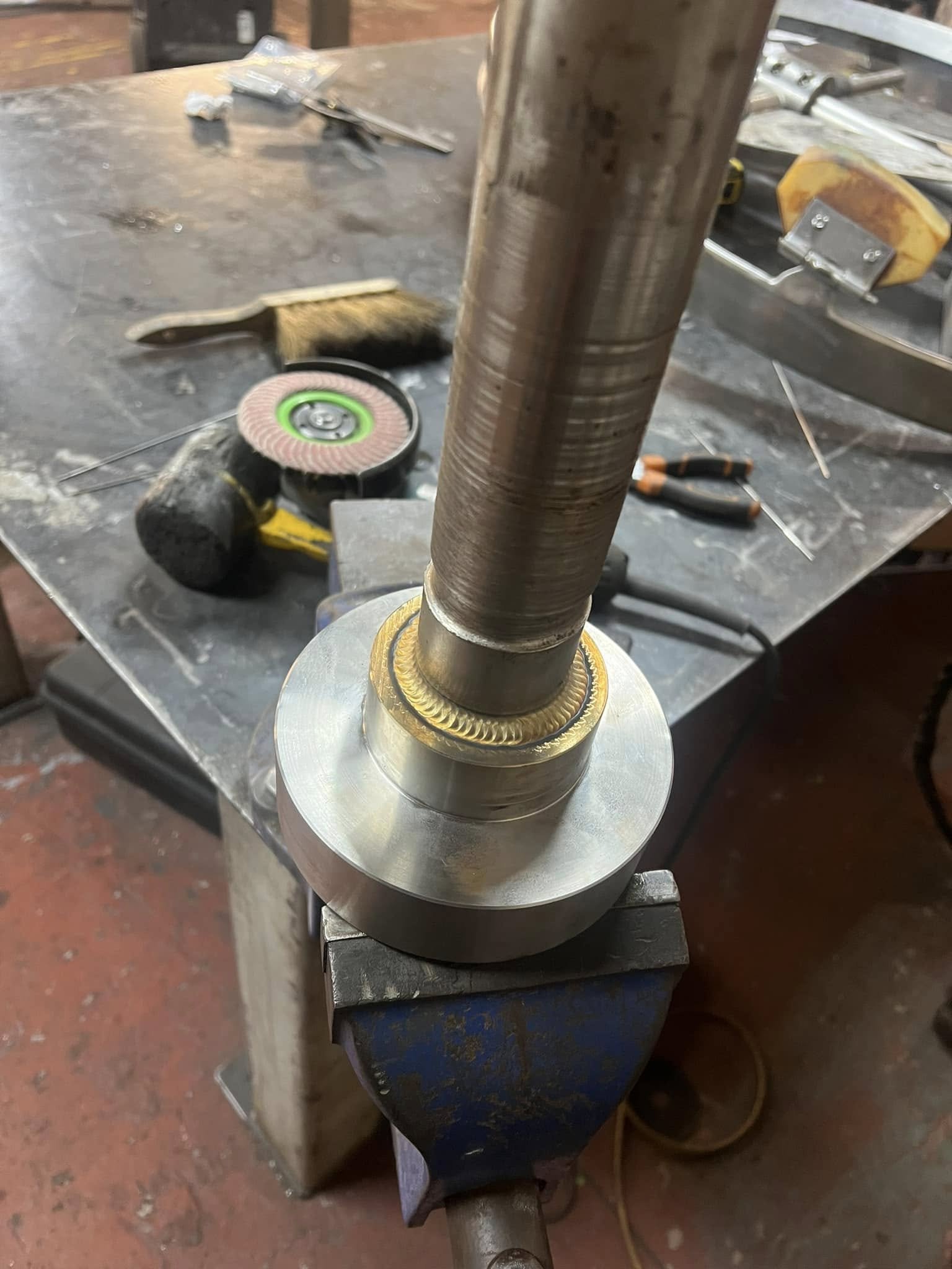 Close-up view of a metal workpiece on a workbench with tools and equipment around, including a grinder, screwdrivers, and a measuring tape.