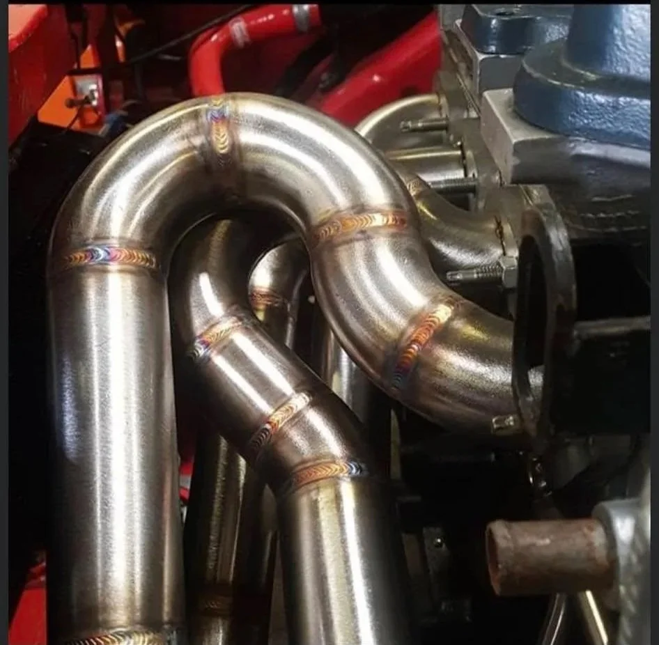 Close-up of shiny metal exhaust pipes with weld marks in a mechanical or automotive setting.