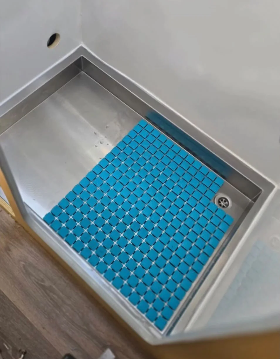 Close-up of a metal sink with a blue anti-slip mat at the bottom, located in a room with white walls and a wooden floor.