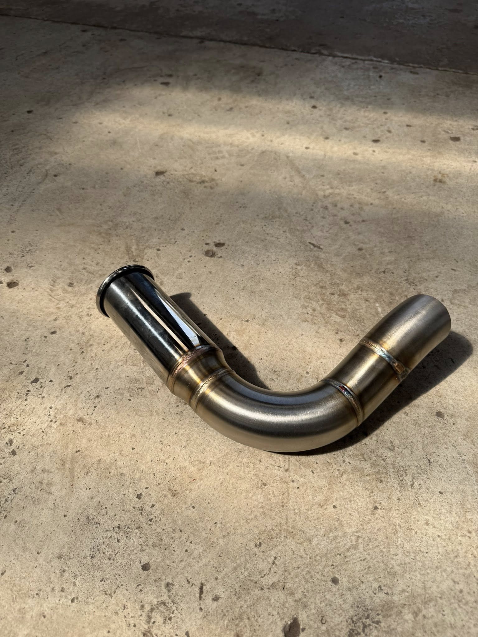 A metallic exhaust pipe laying on a concrete surface.
