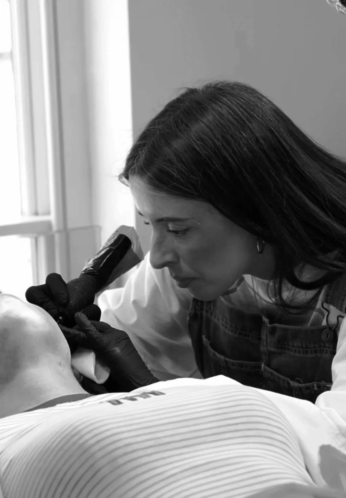 A woman in a lab coat examining a patient's head with a microscope in a clinical setting.