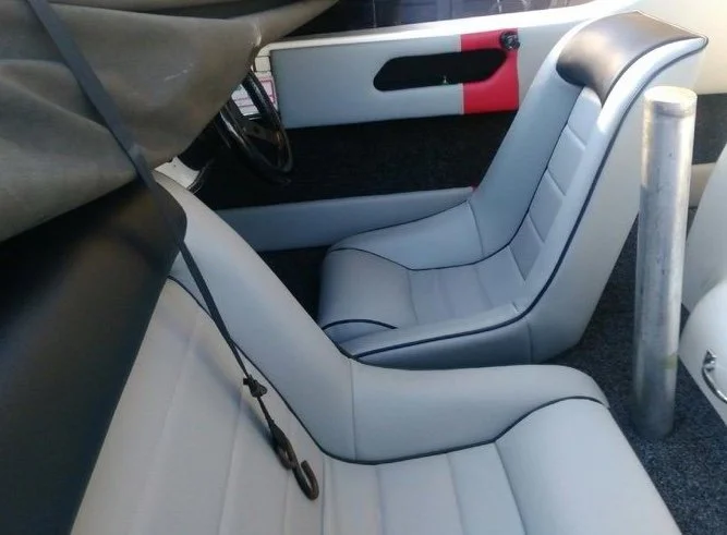 View of two white seats inside a race car, with a red and black door panel and a silver pole next to the seat.