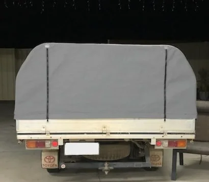Rear view of a small light-colored utility trailer with a gray tarp cover, parked on a concrete surface.