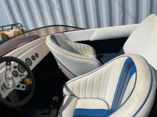 Interior of a boat with white and blue cushioned seats and a steering wheel.
