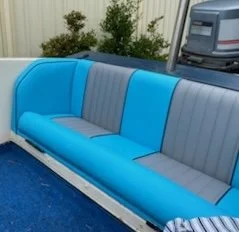 Outdoor blue and gray striped sectional sofa on a concrete patio, with a bush and an outboard motor in the background.