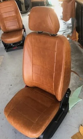 Car seat with brown leather upholstery placed on the floor next to other car seats.