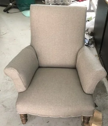 A beige upholstered armchair with wooden legs in a garage or storage area.