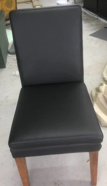 Black upholstered chair with wooden legs in a room with concrete floor and various objects.