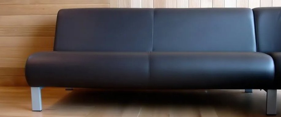 A black leather sofa with metal legs against a wooden-paneled wall.