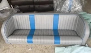 A vintage-style striped sofa with a curved design, featuring blue, gray, and white colors, placed indoors on a concrete floor.