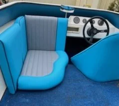 Interior view of a vintage blue convertible car, showing blue and gray upholstered seats, steering wheel, and dashboard.