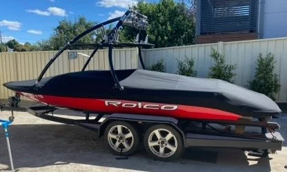 A black and red watercraft on a trailer in a backyard with a beige fence and green trees.