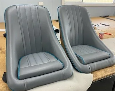 Two gray airplane-style seats on a workbench in a workshop.