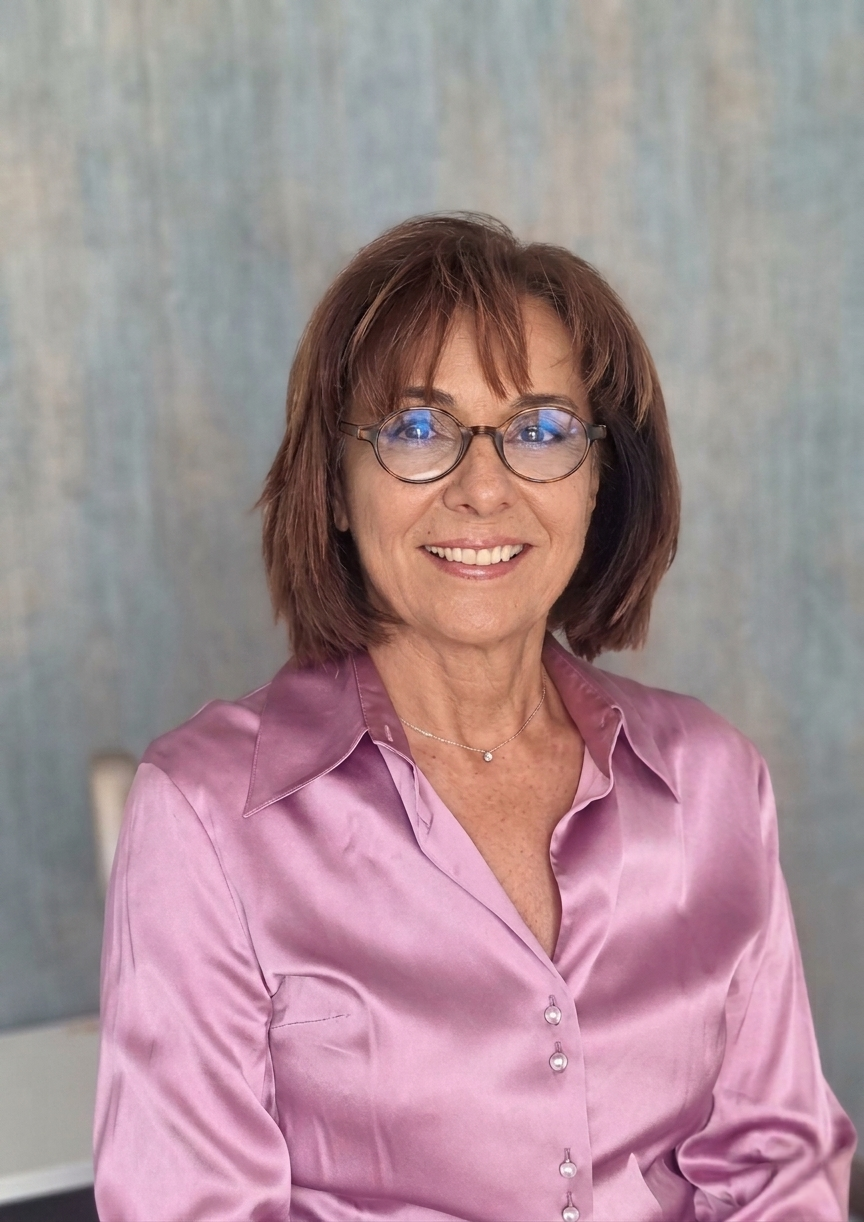 Femme aux lunettes, portant une chemise en satin rose, souriant, fond neutre.
