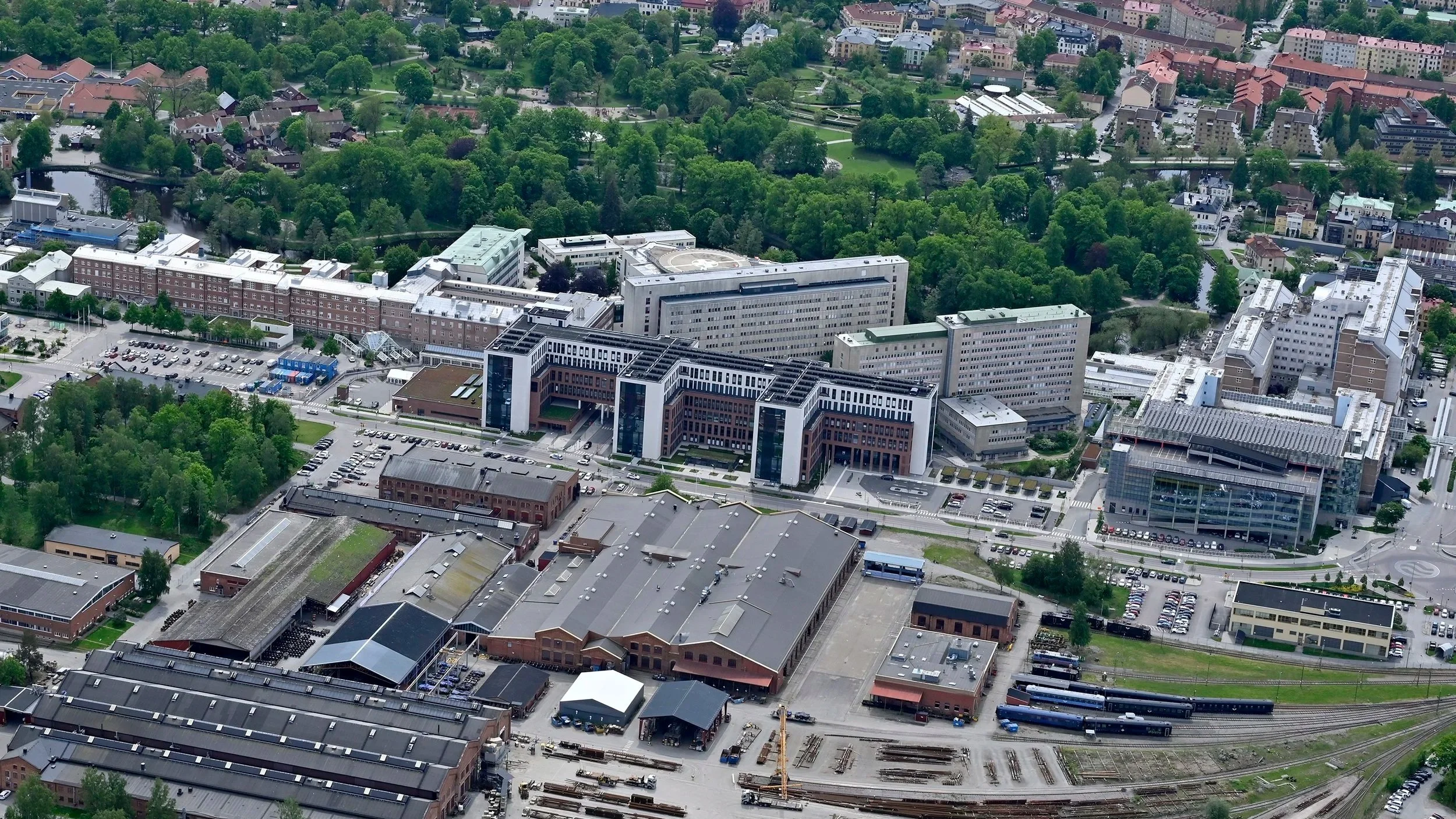 Aerial view of a city with a mix of modern and historic buildings, green parks, and a railway yard with train tracks.