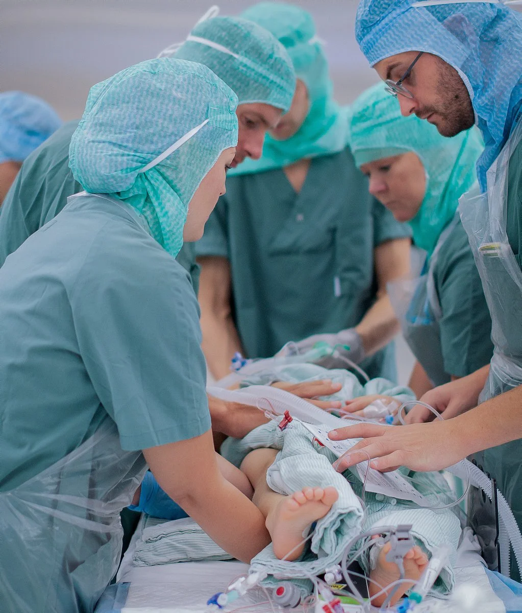 Medical team in surgical gowns and caps performing surgery on a newborn baby in an operating room.